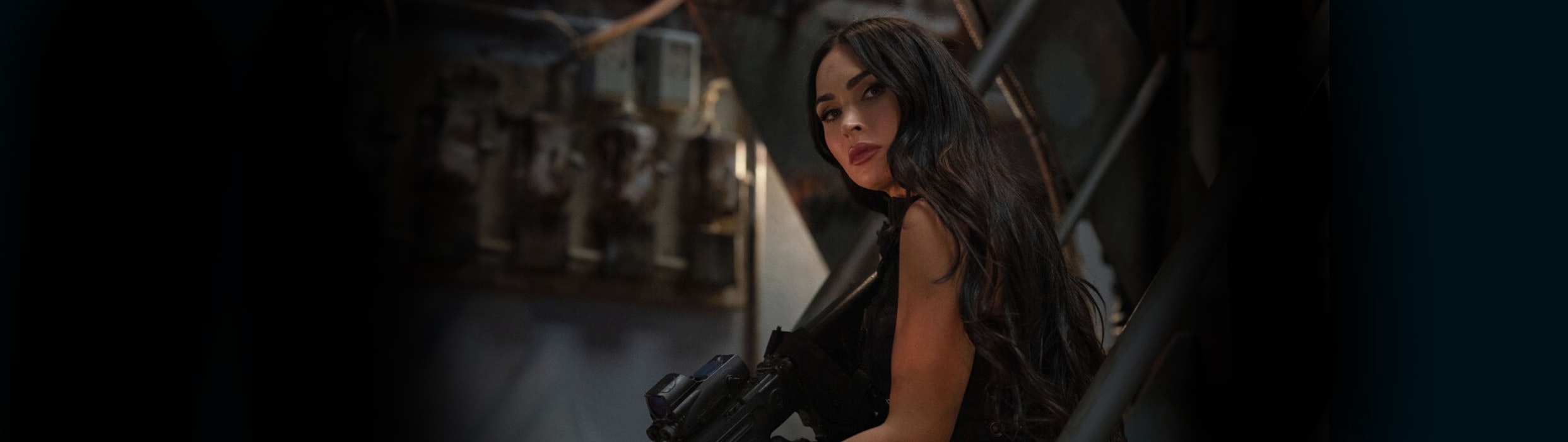 Megan Fox looks at the enemy in a stairwell with a rifle in Expend4bles now showing at Harkins! Get your tickets today!